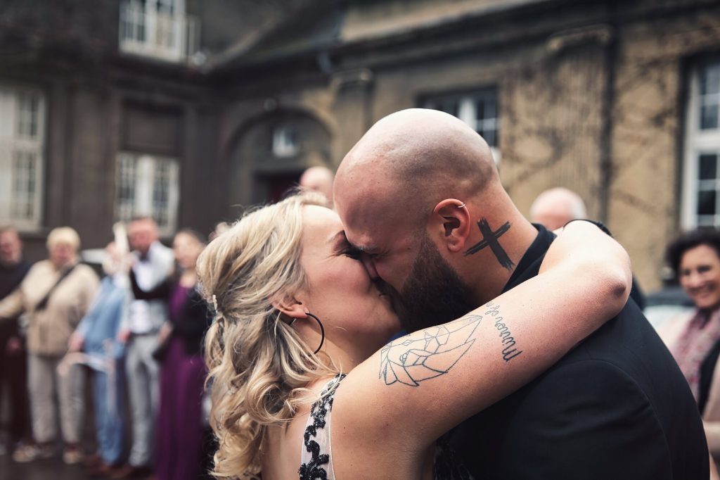 Hochzeitsfotografie – Brautpaar im Kuss umringt von der Hochzeitsgesellschaft, feierlicher Moment, Neografie Ruhrgebiet